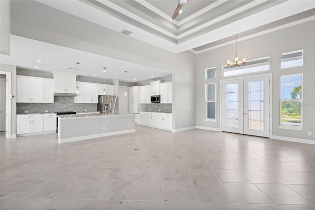 kitchen featuring a tray ceiling, an island with sink, a towering ceiling, an inviting chandelier, and stainless steel appliances