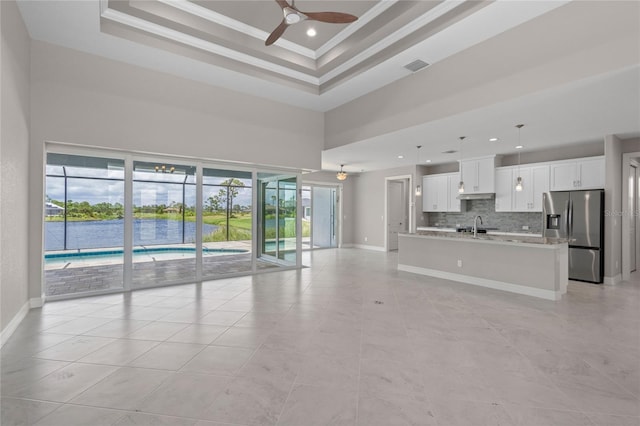 unfurnished living room with sink, ornamental molding, a tray ceiling, ceiling fan, and a high ceiling