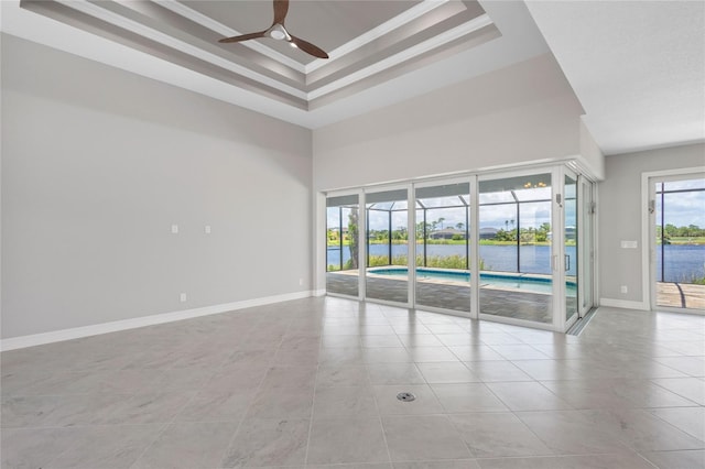 spare room featuring a water view, a towering ceiling, ceiling fan, a tray ceiling, and light tile patterned floors