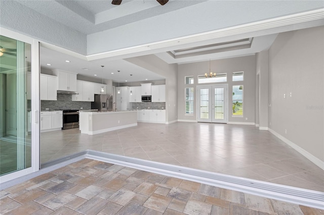 unfurnished living room featuring a tray ceiling, a high ceiling, french doors, and ceiling fan with notable chandelier