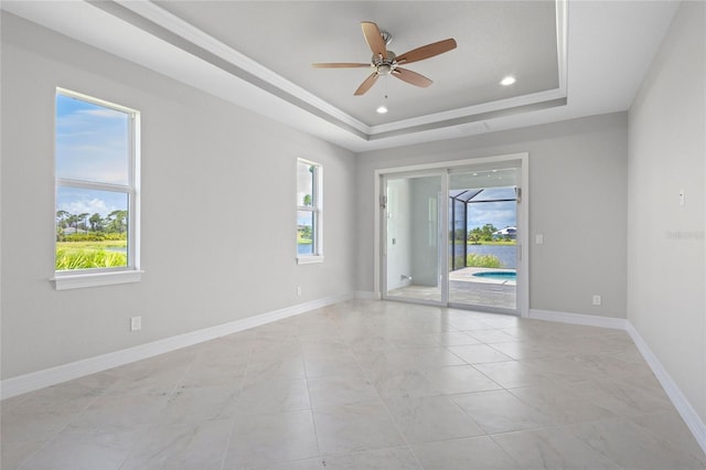 unfurnished room with a raised ceiling, a wealth of natural light, and ceiling fan