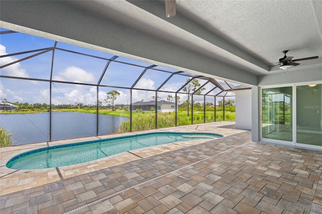 view of swimming pool featuring a patio area, a water view, ceiling fan, and glass enclosure