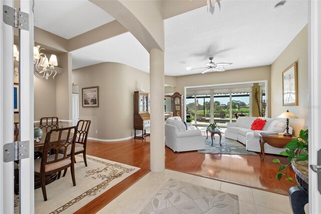 living room with light wood-type flooring and ceiling fan with notable chandelier