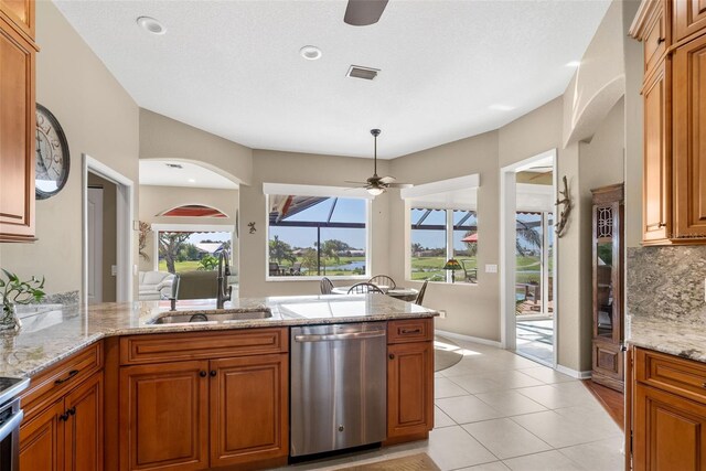 kitchen with light tile patterned floors, sink, light stone countertops, stainless steel dishwasher, and ceiling fan