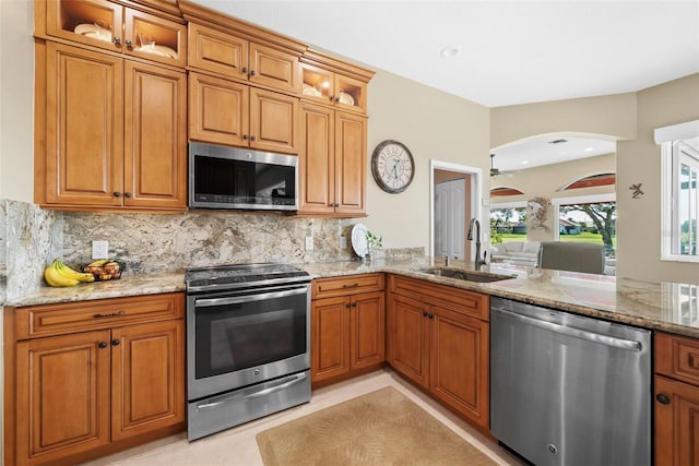 kitchen featuring brown cabinetry, appliances with stainless steel finishes, light stone counters, and a sink