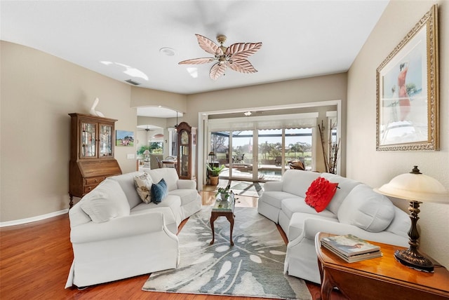 living area featuring baseboards, visible vents, a ceiling fan, arched walkways, and wood finished floors