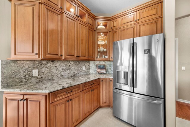 kitchen with tasteful backsplash, light tile patterned flooring, stainless steel fridge, and light stone counters