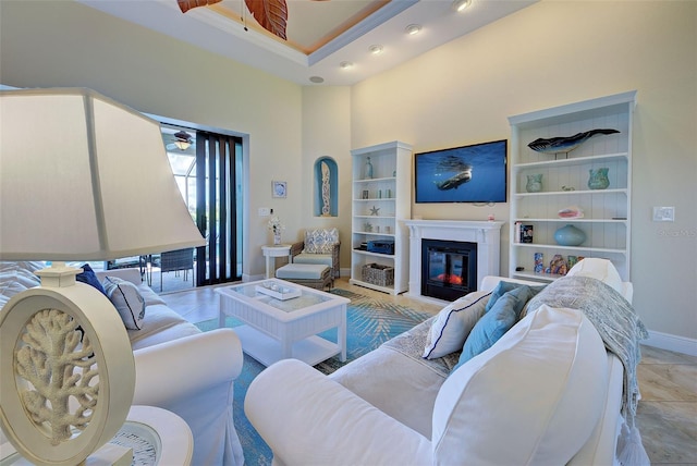 living room featuring a high ceiling, baseboards, a ceiling fan, and a glass covered fireplace