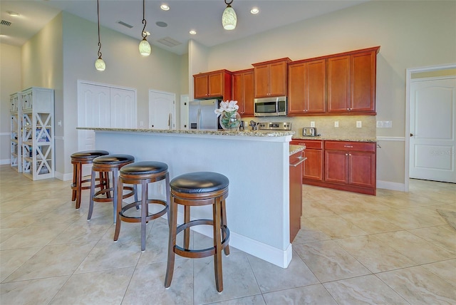 kitchen with a center island with sink, a breakfast bar area, hanging light fixtures, stainless steel appliances, and backsplash