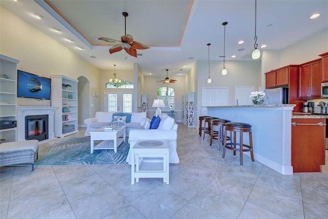 living room featuring light tile patterned floors, arched walkways, a ceiling fan, a glass covered fireplace, and a tray ceiling