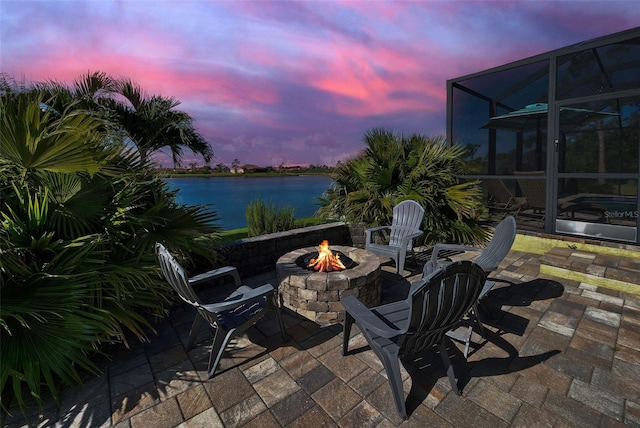 view of patio featuring a water view, glass enclosure, and an outdoor fire pit