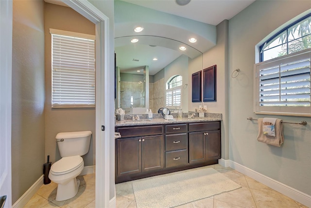 full bath featuring double vanity, baseboards, tiled shower, toilet, and a sink