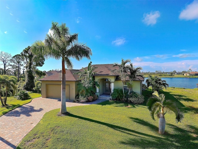 view of front of house featuring an attached garage, a water view, decorative driveway, stucco siding, and a front lawn