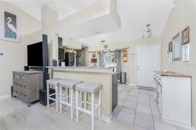 kitchen with kitchen peninsula, white cabinetry, light tile patterned floors, and a breakfast bar area