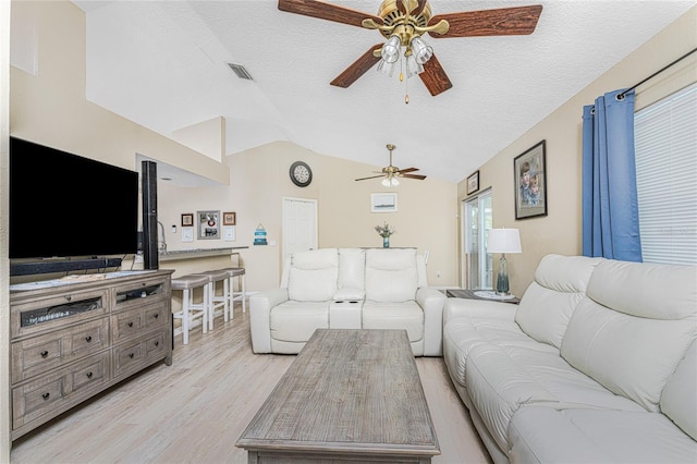 living room featuring ceiling fan, light wood-type flooring, a textured ceiling, and lofted ceiling