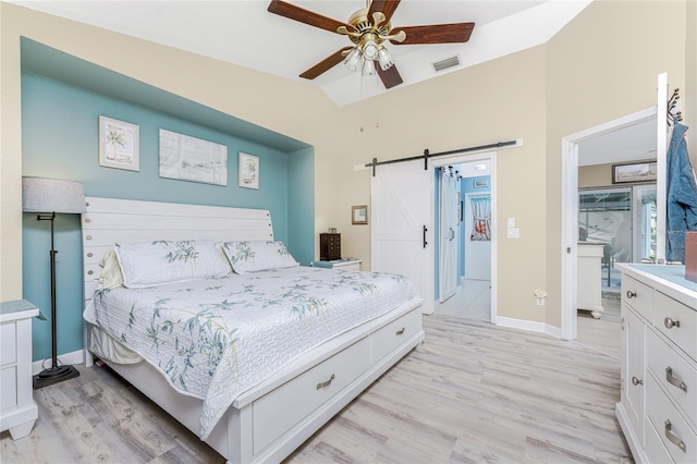 bedroom with ceiling fan, light hardwood / wood-style floors, vaulted ceiling, and a barn door