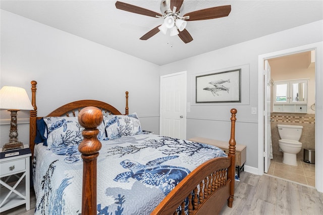 bedroom featuring light hardwood / wood-style floors, connected bathroom, ceiling fan, and tile walls