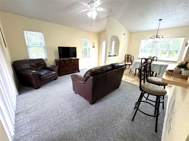 carpeted living room with ceiling fan with notable chandelier, vaulted ceiling, and a textured ceiling