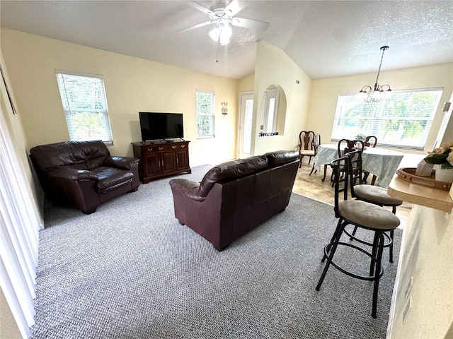 living area with carpet flooring, ceiling fan with notable chandelier, a textured ceiling, and vaulted ceiling