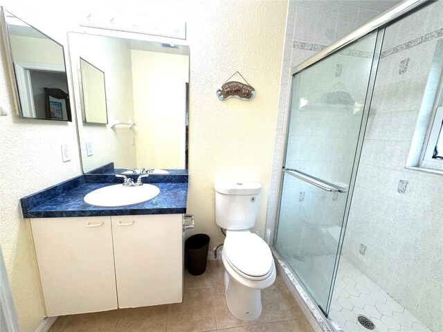 bathroom featuring toilet, vanity, walk in shower, and tile patterned floors