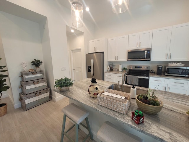 kitchen with appliances with stainless steel finishes, light wood-type flooring, a kitchen breakfast bar, decorative light fixtures, and white cabinetry