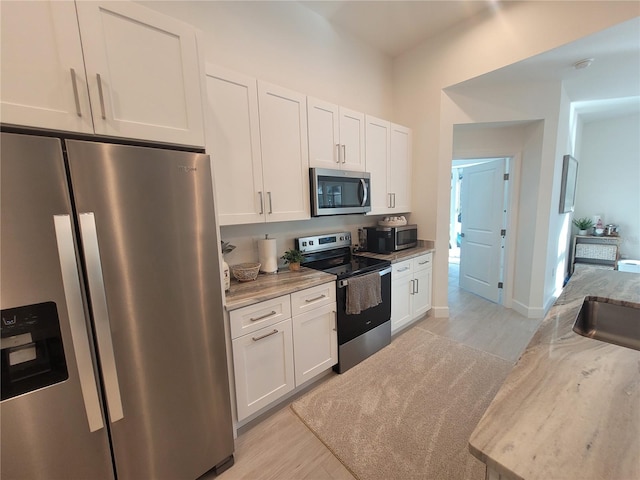 kitchen with white cabinets, stainless steel appliances, light stone countertops, and light hardwood / wood-style floors