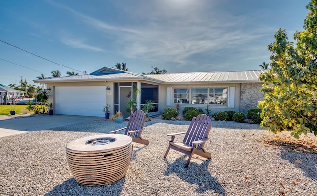 single story home featuring metal roof, stone siding, a garage, a fire pit, and concrete driveway