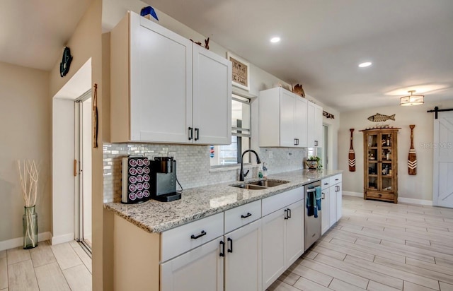 kitchen featuring tasteful backsplash, dishwasher, light stone counters, white cabinetry, and a sink