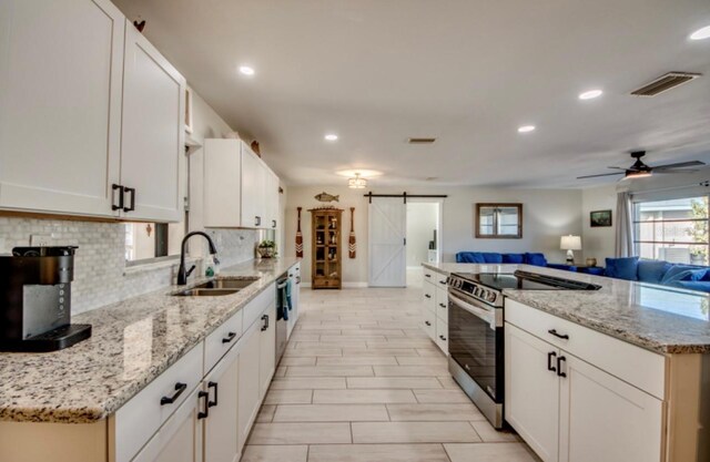 kitchen with a barn door, stainless steel electric range oven, sink, and white cabinetry