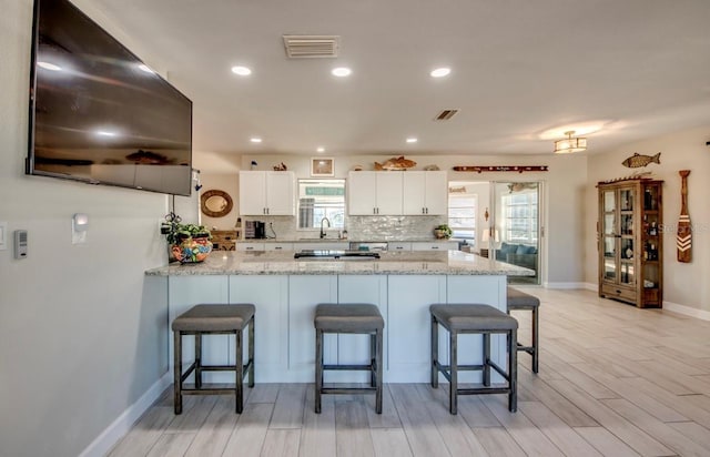 kitchen with visible vents, white cabinetry, backsplash, a peninsula, and light stone countertops