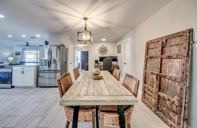 dining space with ceiling fan with notable chandelier and light wood-type flooring