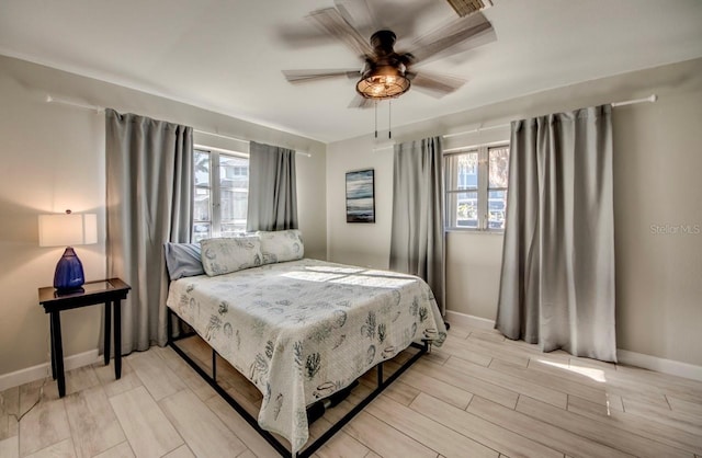 bedroom featuring wood finish floors, multiple windows, a ceiling fan, and baseboards