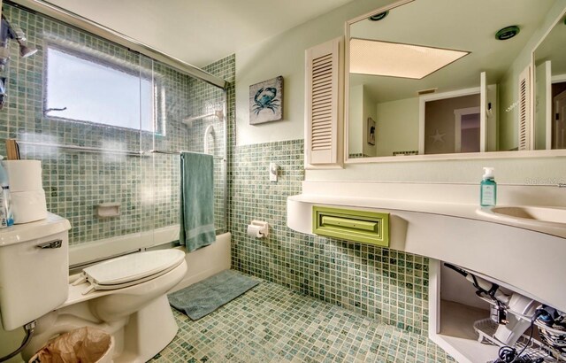 full bathroom featuring tile patterned floors, combined bath / shower with glass door, sink, toilet, and tile walls