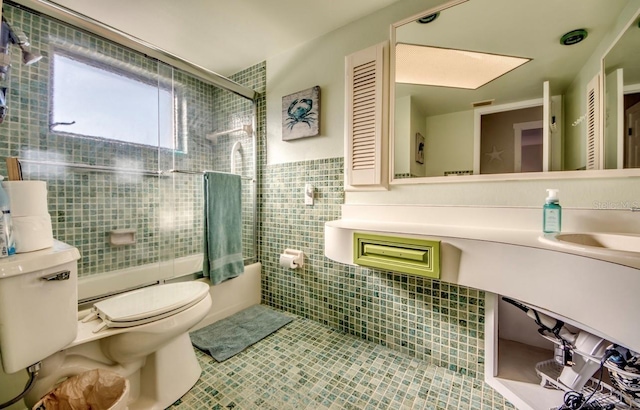 bathroom featuring tile patterned flooring, toilet, shower / bath combination with glass door, a sink, and tile walls