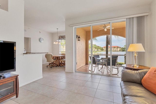 living area with light tile patterned flooring, a water view, baseboards, and ceiling fan with notable chandelier