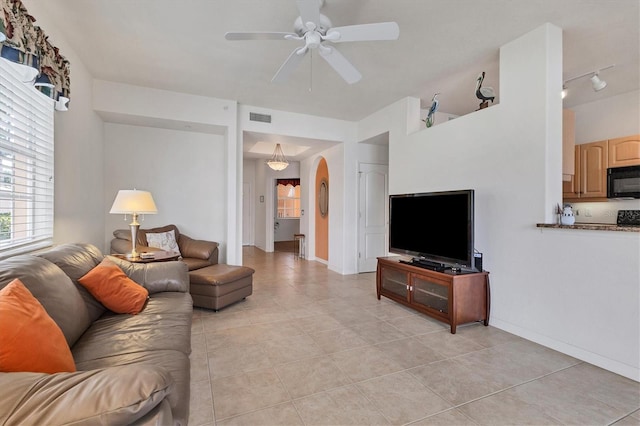 living area with arched walkways, light tile patterned floors, visible vents, ceiling fan, and baseboards