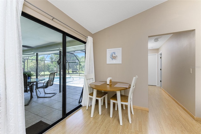 dining area with a sunroom, vaulted ceiling, light wood-style flooring, and baseboards