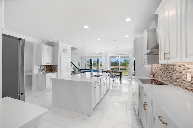 kitchen with an island with sink, stainless steel fridge, range hood, and backsplash