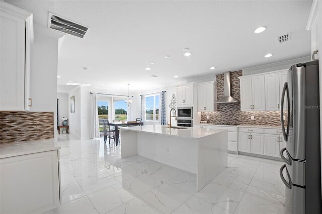 kitchen with a center island with sink, tasteful backsplash, stainless steel appliances, wall chimney range hood, and white cabinets