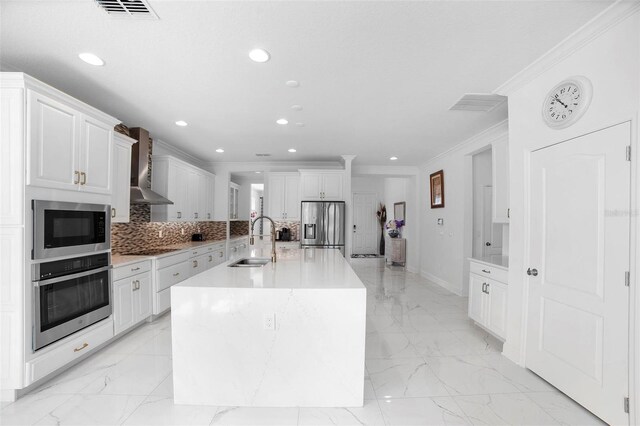 kitchen featuring stainless steel appliances, sink, wall chimney exhaust hood, a center island with sink, and white cabinets