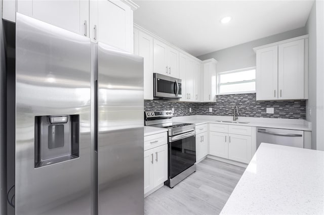 kitchen featuring light hardwood / wood-style floors, sink, tasteful backsplash, appliances with stainless steel finishes, and white cabinets