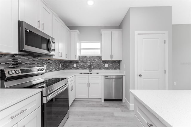 kitchen featuring sink, backsplash, light hardwood / wood-style floors, stainless steel appliances, and white cabinets