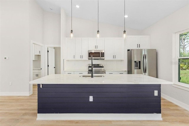 kitchen featuring light hardwood / wood-style flooring, an island with sink, white cabinetry, appliances with stainless steel finishes, and light stone counters