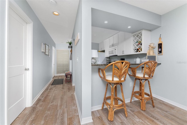 kitchen with white cabinetry, a breakfast bar area, light wood finished floors, baseboards, and white microwave