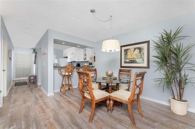 dining room featuring an inviting chandelier, light wood-style flooring, baseboards, and a textured ceiling