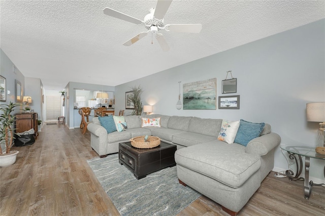 living room with baseboards, a textured ceiling, wood finished floors, and a ceiling fan