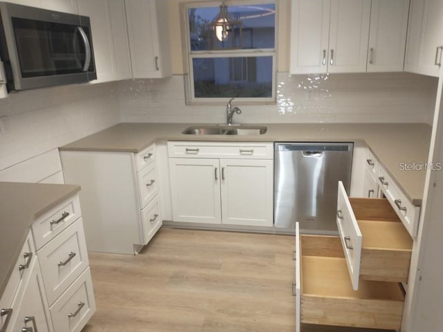 kitchen with stainless steel appliances, sink, decorative backsplash, white cabinets, and light hardwood / wood-style floors