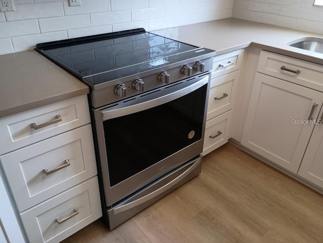 kitchen with electric range, light wood-type flooring, white cabinetry, and tasteful backsplash