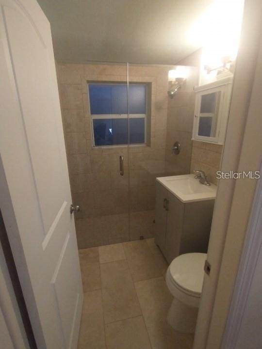 bathroom with tile patterned flooring, vanity, a shower with shower door, and toilet