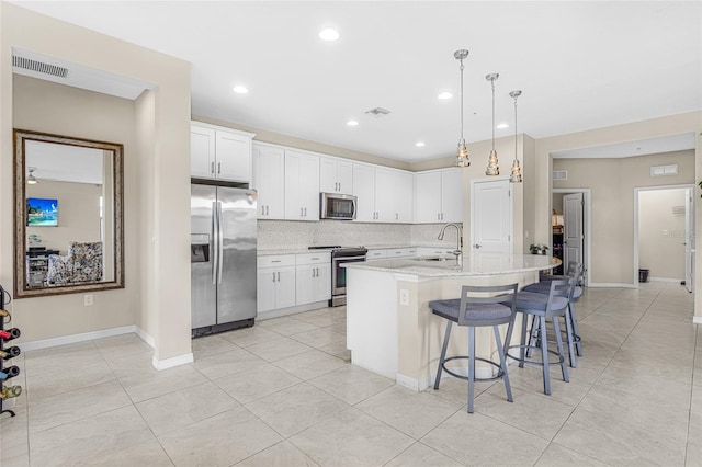 kitchen with backsplash, stainless steel appliances, white cabinetry, an island with sink, and light tile patterned flooring